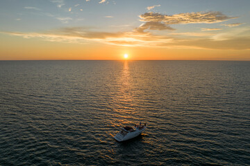 Aerial view of unrecognizable people having fun on white yacht at sunset floating on sea waves with ripple surface. Motor boat recreation on ocean surface