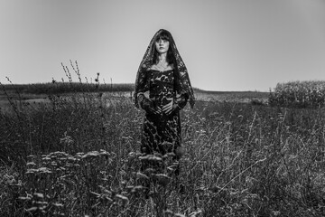Grayscale of a young mourning woman with bangs in a black dress in a field