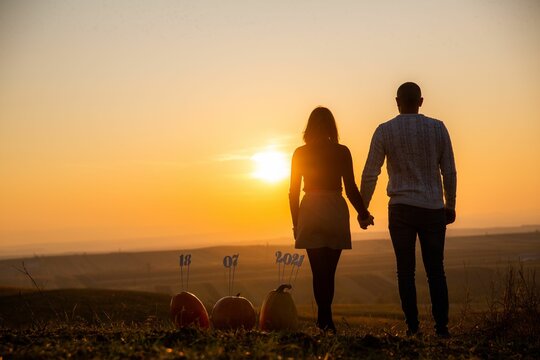 Cute couple holding hands at sunset with their marriage date in the background