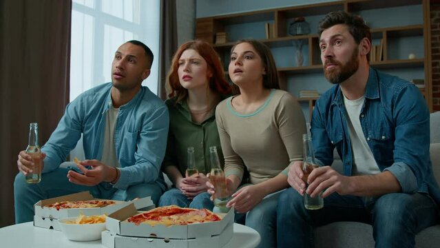 Multiethnic friends watch television with beer pizza on home sofa diverse men women supporters watching TV sport game match soccer football fans worried sad disappointed by failure team losing no goal