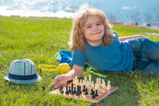 Chess school outdoor. Child think or plan about chess game, laying on grass in summer park. Intelligent, smart and clever school kids. Logic game for kids and logical thinking.