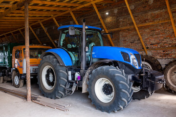 A new modern blue tractor is parked in a farm hangar.