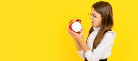 shocked kid in school uniform and glasses looking at alarm clock showing time, copy space, deadline. Teenager child with clock alarm, horizontal poster. Banner header, copy space.