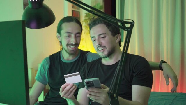 Young long haired Latin man trying to convince his friend of an online purchase via his cell phone with credit card.
