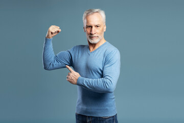 Strong gray haired senior man showing muscles looking at camera isolated on blue background....