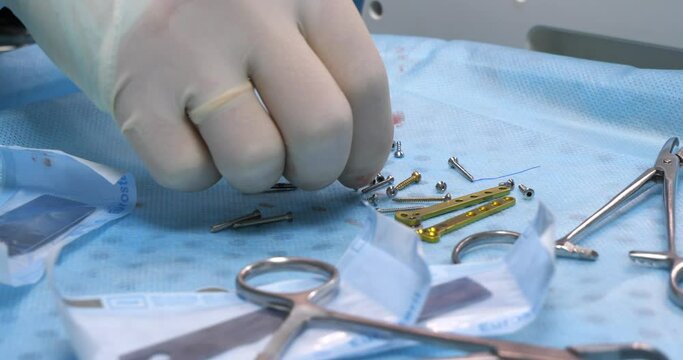 In the operating room, the hand of a veterinary surgeon puts down a medical drill and begins to choose screws to secure a titanium plate to a broken bone. Close-up. Veterinary traumatology.