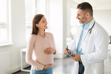 Doctor's appointment. Happy young pregnant woman talking with het therapist during medical check up in office