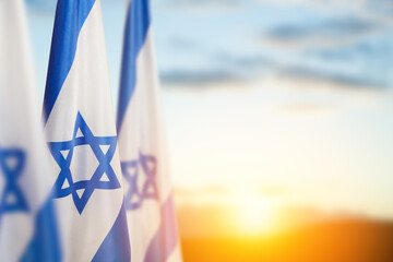Fototapeta premium Israel flags with a star of David over cloudy sky background on sunset. Banner with place for text.