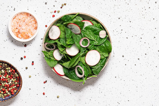 Fresh juicy salad with baby spinach leaves, small radish and onion on white stone table top view.