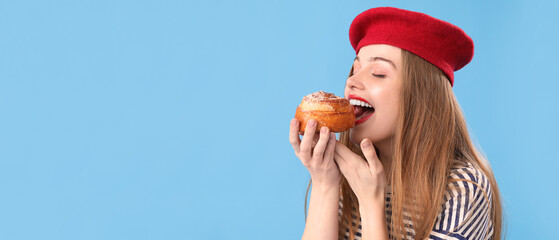 Young woman eating tasty bun on blue background with space for text