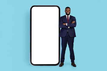Business Advertisement. Handsome Black Businessman Standing Near Huge Blank Smartphone
