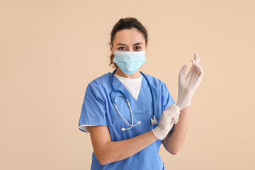 Female medical assistant putting on rubber gloves against beige background