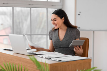 Female accountant working with document and calculator at table in office