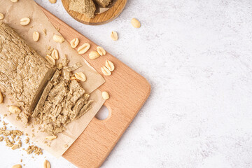 Wooden board of sweet halva with peanuts on light background