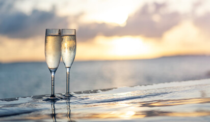 Two glasses of champagne on the side of the infinity pool against the backdrop of a sunset in the...