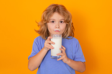 Little child drinking milk. Kid with glass of milk on yellow isolated background.