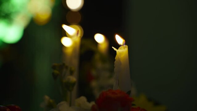 Air blows out flame of one burning paraffin candle in dark hall with colored illumination. Smoke rises above smoldering wick, flames of other candles sway in wind, backlight changes color.