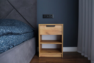 Close-up fragment of bedroom with empty wooden bedside table in a gray bedroom.