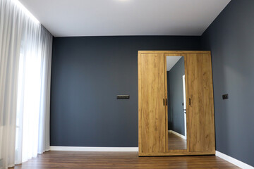 A wooden wardrobe with a mirror. Modern bedroom interior in gray tones. White ceiling and laminate flooring.	