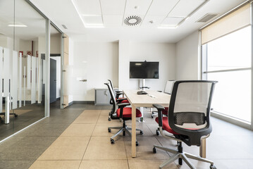 Fototapeta na wymiar A spacious office with glass partitions with several swivel chairs with a red seat, a wooden table