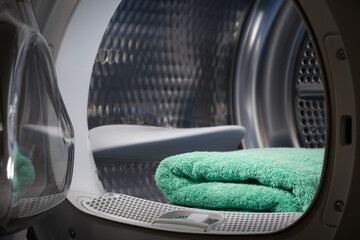 Turquoise towel are stacked in the tumble dryer. Laundry. Clean concept. Washing machine with open...
