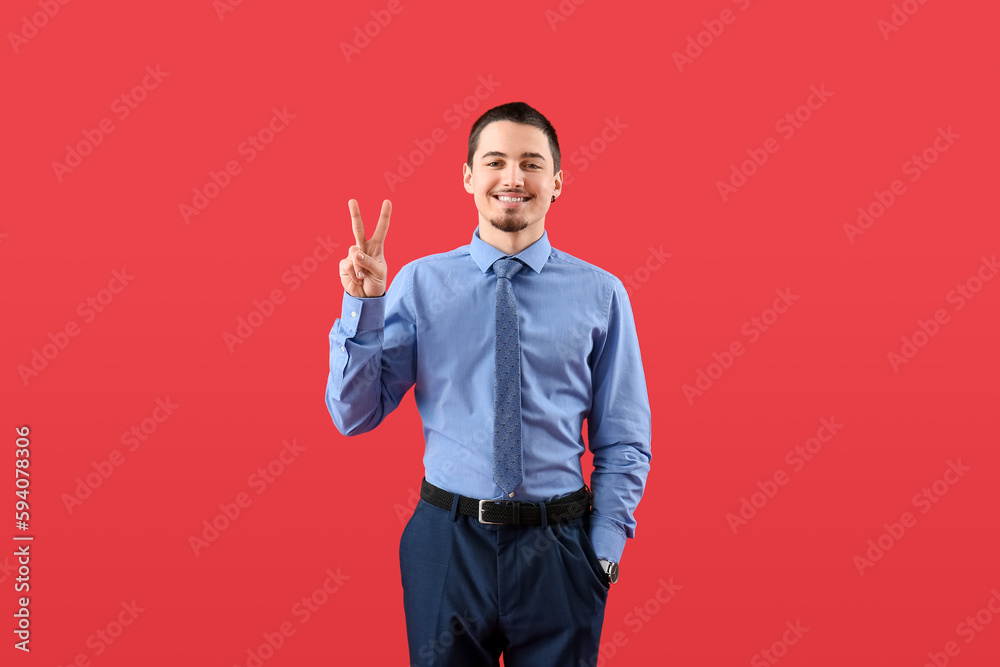 Wall mural Handsome businessman showing victory gesture on red background