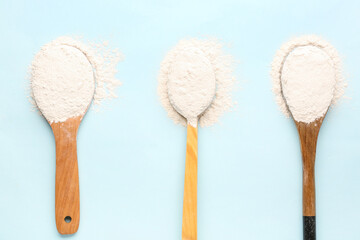 Different wooden spoons with wheat flour on blue background, closeup