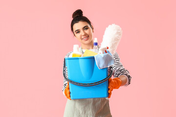 Young woman with cleaning supplies  on pink background