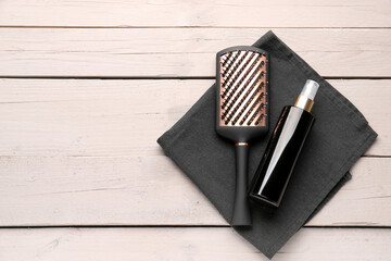Hair brush with spray bottle and towel on light wooden background
