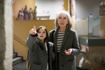 Cute interested preteen girl visiting museum of applied arts with grandmother, exploring ancient...