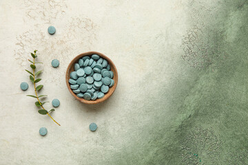 Bowl with pills and eucalyptus branch on grunge background
