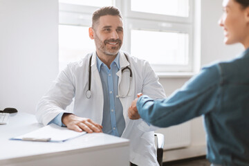 Medical services concept. Male doctor and female patient handshaking during meeting in clinic