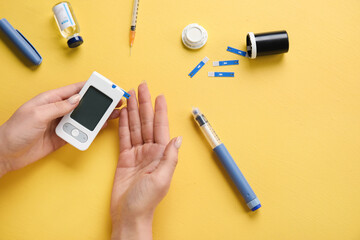 Diabetic woman with digital glucometer, lancet pen and insulin on yellow background
