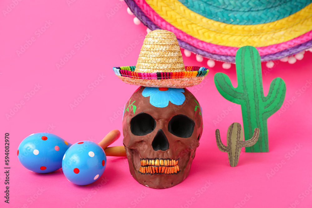 Wall mural Mexican maracas, painted skull with sombrero hats and paper cacti on pink background