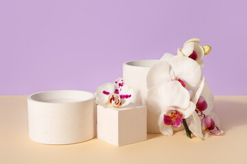 Decorative plaster podiums and beautiful orchid flowers on beige table against lilac background