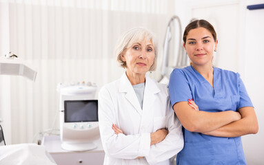Obraz premium Two smiling woman doctors posing against background of cosmetology devices in aesthetic clinic