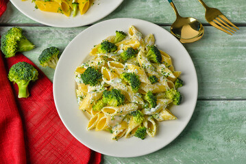Plate with tasty pasta and broccoli on green wooden background