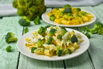 Plate with tasty pasta and broccoli on green wooden background