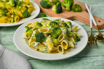 Plate with tasty pasta and broccoli on green wooden background