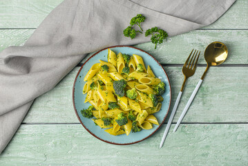 Plate with tasty pasta and broccoli on green wooden background