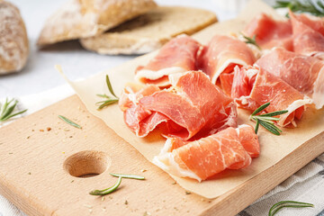 Wooden board with slices of tasty jamon on table, closeup