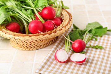 Wicker basket of ripe radish with green leaves on light tile background, closeup