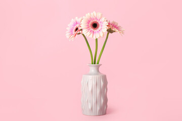 Vase with gerbera flowers on pink background