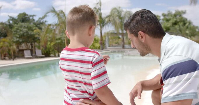 Happy caucasian father and son talking at swimming pool at beach house