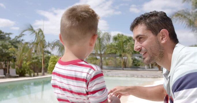 Happy caucasian father and son talking at swimming pool at beach house