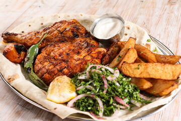 Half grilled chicken with salad, wedges, lemon and dip served in dish isolated on background top view of arabic food