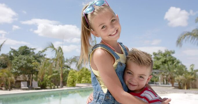 Portrait of happy caucasian siblings embracing at swimming pool at beach house