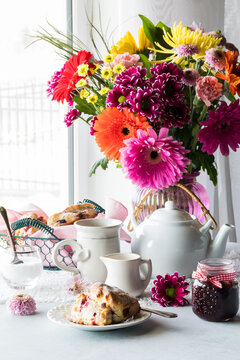An arrangement of tea and scones with a beautiful flower bouquet in behind.