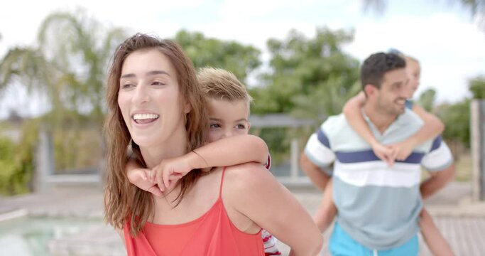 Happy caucasian parents carrying children at swimming pool at beach house