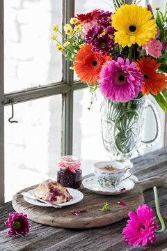 A rustic scene of tea and a scone served with jam with pretty flowers in behind.